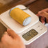 Yellow and gray fabric roll on a digital scale with a person's hand holding it.